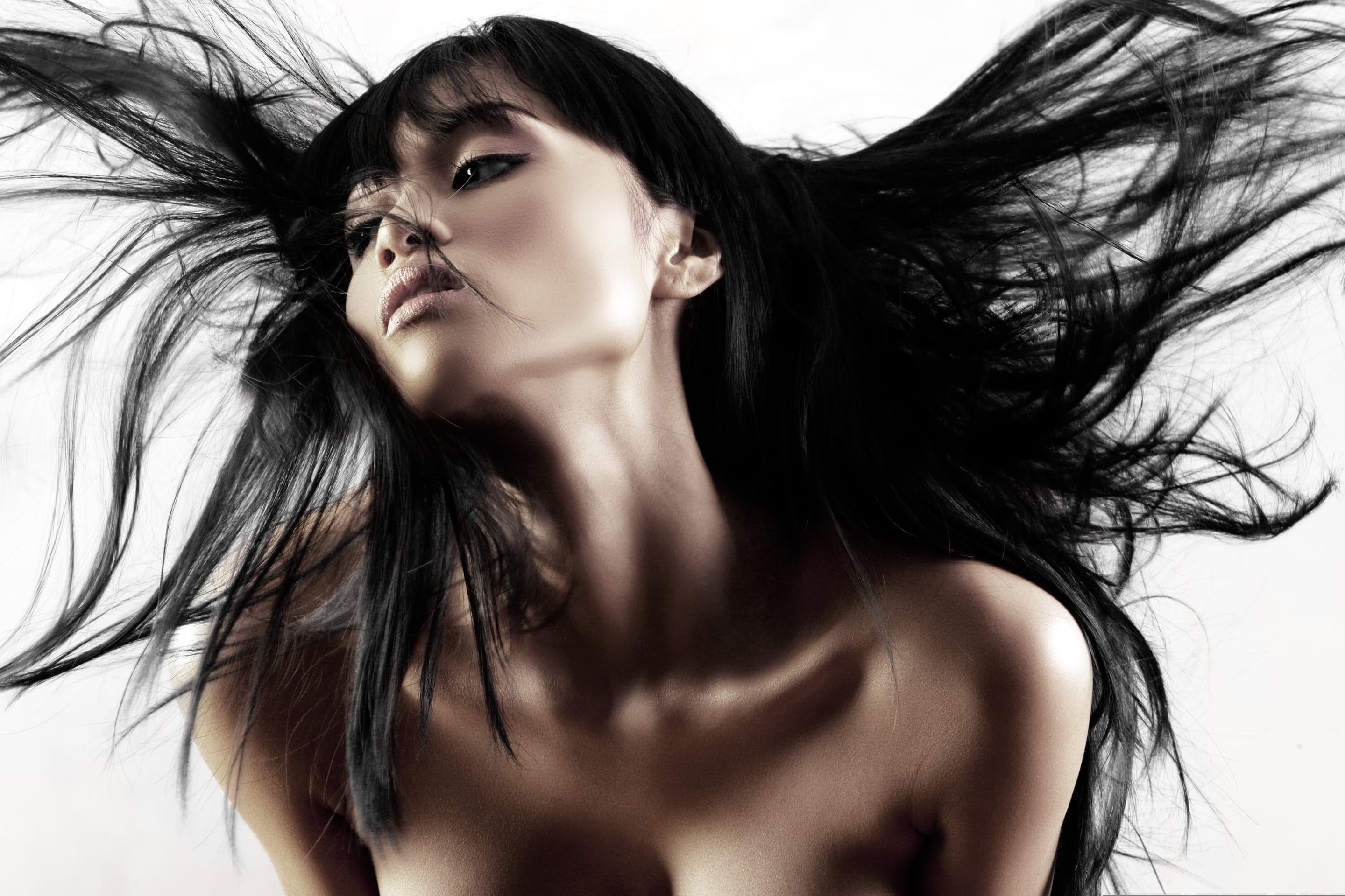 A woman tossing her long black hair against a white backdrop