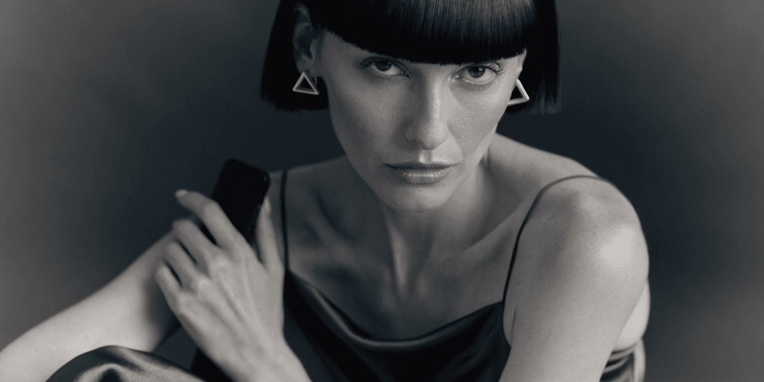 A woman in a black slip dress holding a black HERMA remote against her shoulder